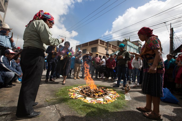 Indigenous leaders light a fire in a sacred circle, arranged on a Guatemala City street. Bystanders look on.