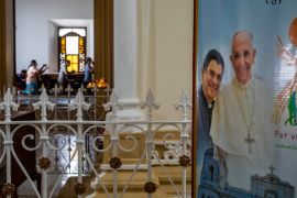 A poster featuring Bishop Rolando Alvarez and Pope Francis hangs inside the Cathedral in Matagalpa, Nicaragua. There are worshippers behind