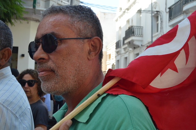 A man in dark sunglasses holds a red Tunisian flag over his shoulder as he marches through the streets of Tunis on October 12.