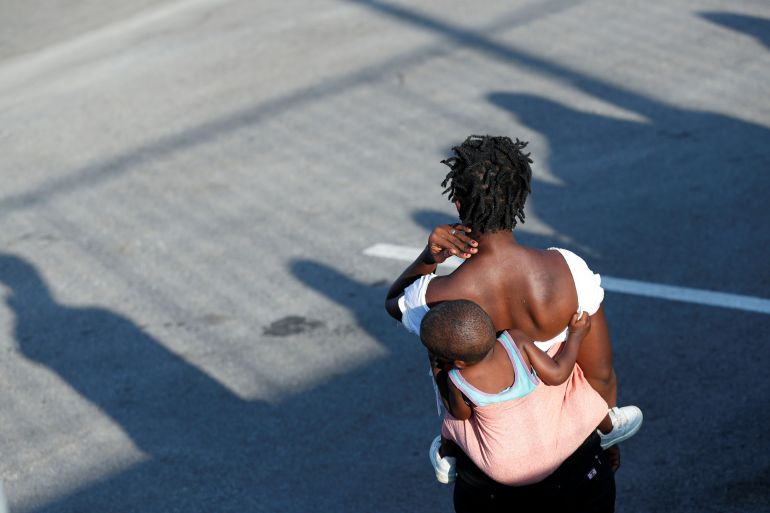 A woman carrying a child on her back waits outside a supermarket near a new temporary camp for migrants and refugees, on the island of Lesbos, Greece, September 19, 2020. REUTERS/Yara Nardi