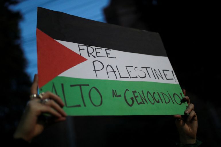 A woman holds a poster that reads "Free Palestine" and "Stop the Genocide" next to other protesters gathered outside the Embassy of Israel during a demonstration in support of the Palestinians, in Mexico City, Mexico