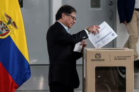 President Gustavo Petro, dressed in a dark suit, puts a ballot into a cardboard box in a nondescript room. The Colombian flag is behind him.