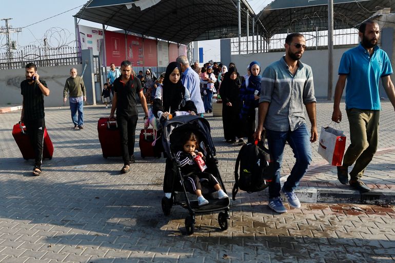 Palestinians with dual citizenship walk as they wait for permission to leave Gaza, amid the ongoing conflict between Israel and Palestinian Islamist group Hamas, at the Rafah border