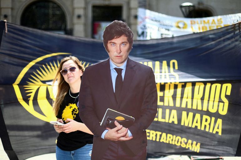 A woman walks past a cardboard cut-out of Javier Milei in a suit and tie.