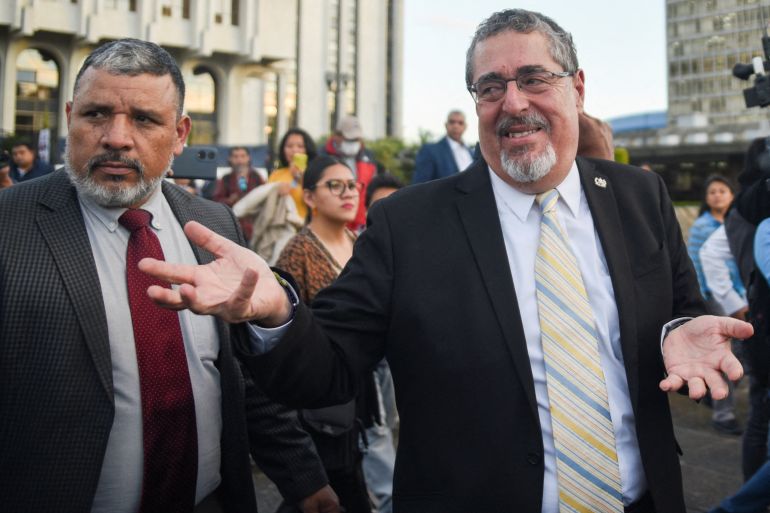 Bernardo Arevalo, dressed in a dark suit and striped tie, gestures in a shrug as he walks outside the Supreme Court in Guatemala City