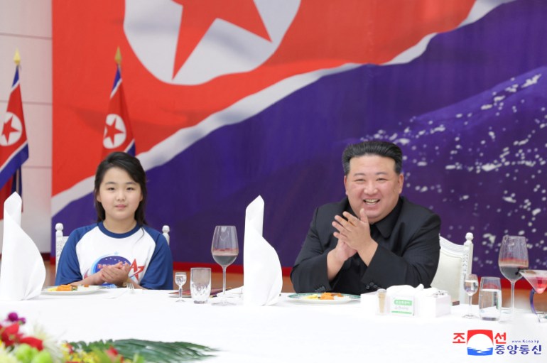 Kim and his daughter seated at the table during the banquey. He is clapping and smiling, She is wearing a T-shirt with the 'NATA' logo on it.