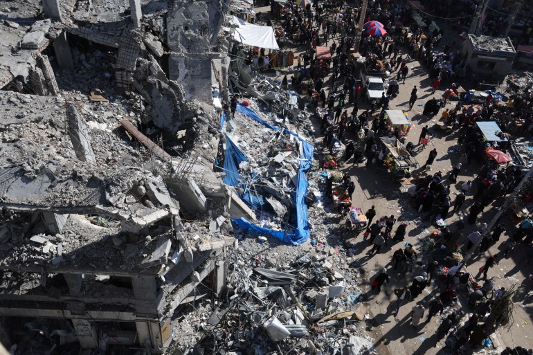 Palestinians shop in an open-air market among the ruins of houses and buildings destroyed in Israeli strikes during the conflict, amid a temporary truce between Hamas and Israel, in Nuseirat refugee camp in the central Gaza Strip