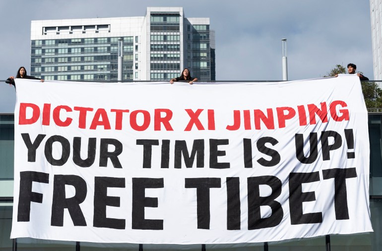 A large banner outside the APEC venue reading 'Dictator Xi Jinping, your time is up! Free Tibet'. It is being held by several Tibetan students