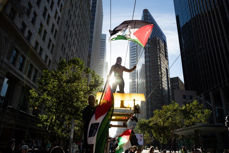 a person holding a Palestinian flag stands against high rise buildings