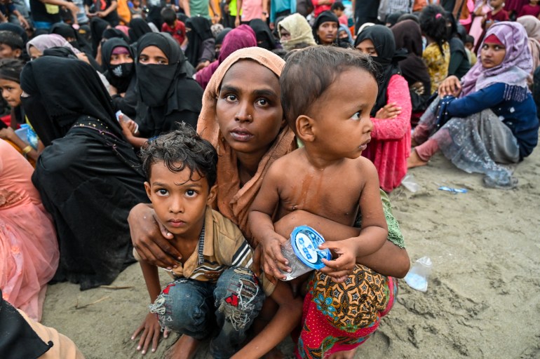 A Rohingya woman holding two young children. Other refugees are behind them