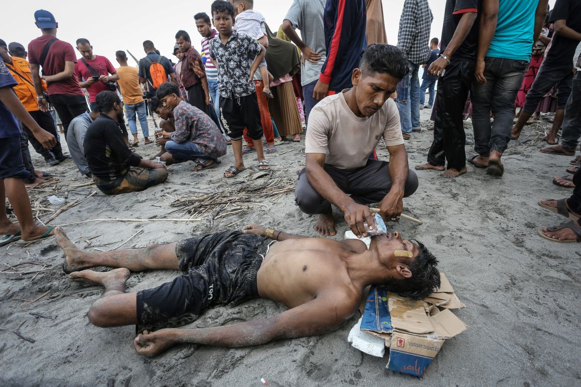 A man gives water to a newly arrived Rohingya refugee after he swam to the beach as others are stranded on a boat after the nearby community decided not to allow them to land but gave them water and food in Pineung, Aceh province.