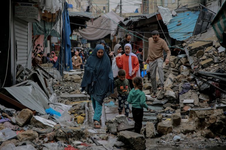 Palestinians walk amid debris of buildings hit in Israeli strikes, near Al-Zawiya market in Gaza City