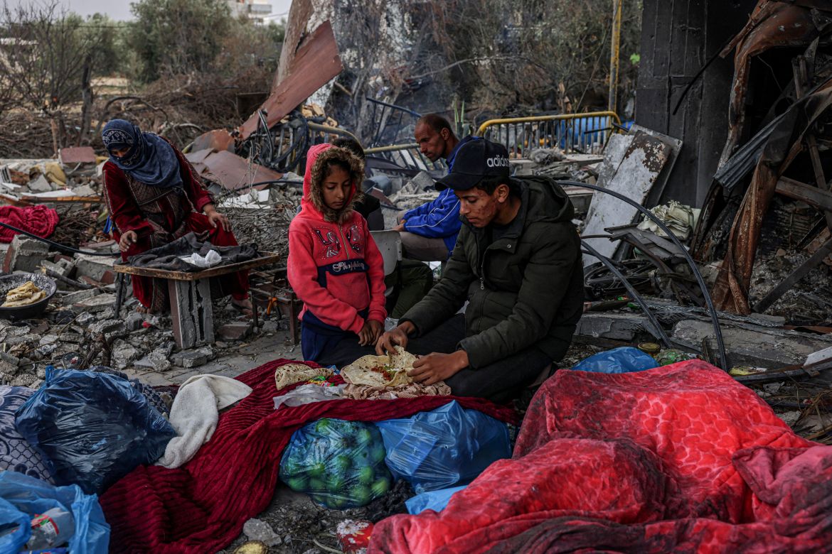Palestinians eat outside amid the destruction caused by Israeli strikes in the village of Khuzaa, east of Khan Yunis near the border fence between Israel and the southern Gaza Strip.