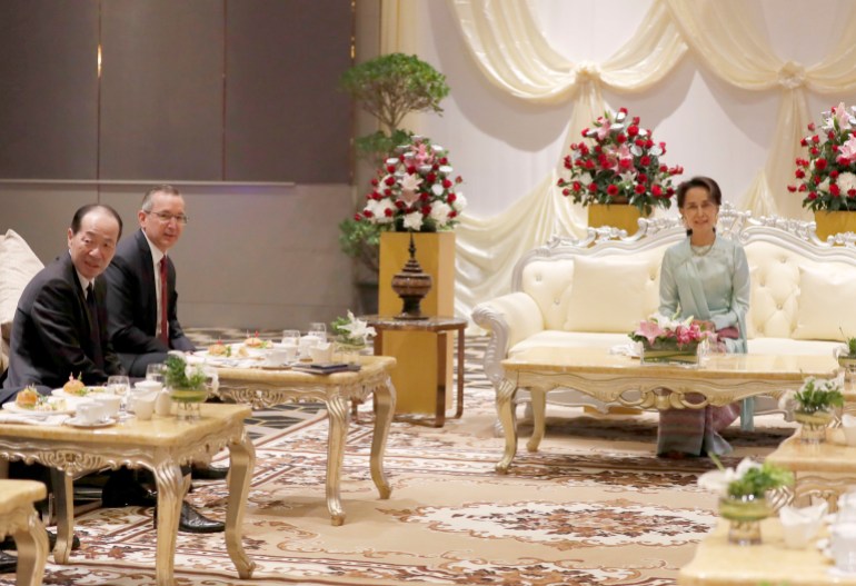 Scot Marciel pictured with Japanese Ambassador to Myanmar Ichiro Maruyama meeting then Myanmar leader Aung San Suu Kyi in 2019. They are sitting in a grand looking room on armchairs to one side. Aung San Suu Kyi is seated on a large white sofa in the middle. There are vases of flowers behind her.