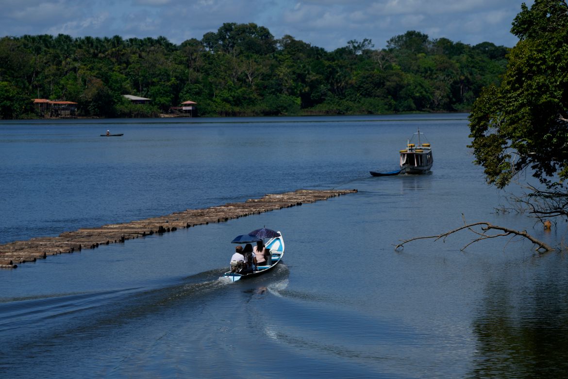 A family travels in a boat shaded by umbrellas next to a boat transporting wooden logs in a section of the Tocantis River, next the island of Tauare, in the municipality of Mocajuba, Para state, Brazil.