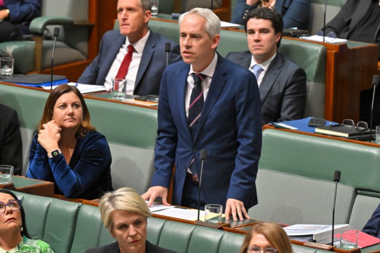 Minister for Immigration Andrew Giles speaking in Australia's parliament. He is standing. Other MPs ate on the benches around him.