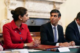 Britain's former home minister Suella Braverman listens to Prime Minister Rishi Sunak. Both are sitting next to each other on a table