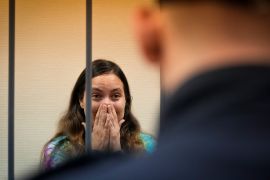 Sasha Skochilenko reacts the verdict. She is standing in the dock and has her hands to ger face covering her nose and mouth A police officer is in front.