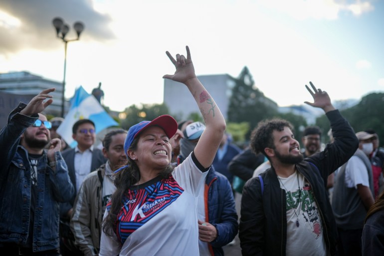 A protester in a baseball cap makes the sign language symbol for love with her raised hand as she joins others on the street in support of Bernardo Arevalo.