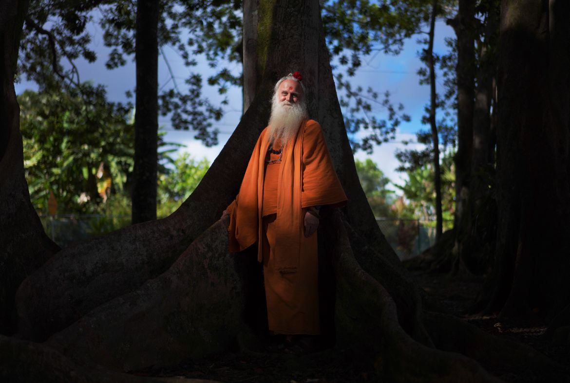 Paramacharya Sadasivanatha Palaniswami stands at the base of a Rudraksha tree, which produces a bright blue fruit at the Kauai Hindu Monastery.