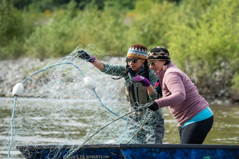 Two women, both wearing knit hats, throw a net into the Klamath River.