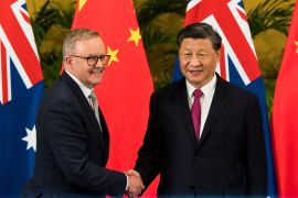two men in suits shake hands in front of the Australian and Chinese flags
