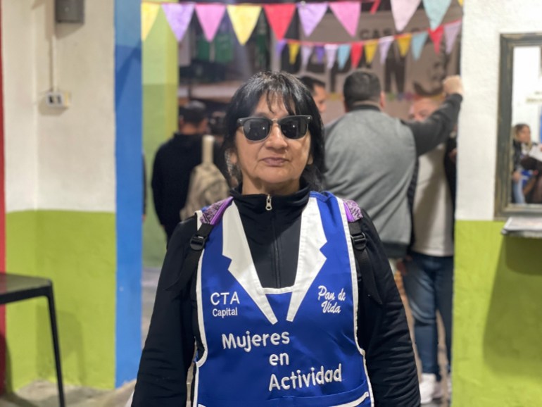 Miriam Liempe, dressed in a blue CTA-branded vest with the words "Mujeres en Actividad" stitched across the front. Behind her, festival, multicoloured banners can be seen down a hallway.