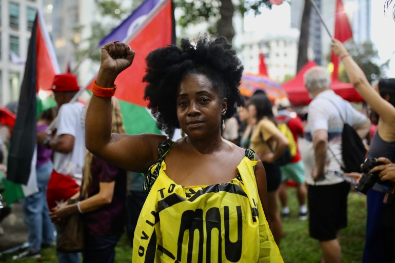A woman who wears a yellow banner tucked into the front of her shirt raises a fist in solidarity at a pro-Palestinian protest in Rio de Janeiro.