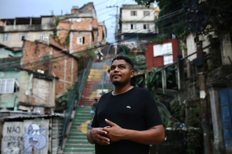 A man in a black T-shirt stands in front of the steps of the favela Morro da Providência.