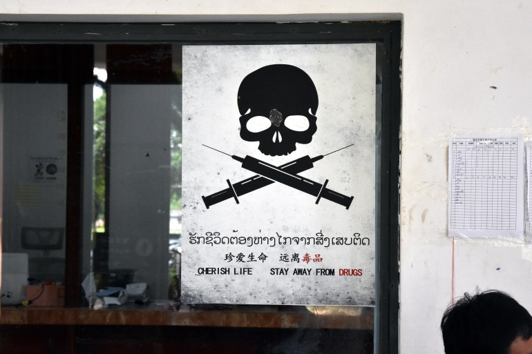 An anti-drugs poster in the Golden Triangle. It depicts s black skull and crossbones on a white background. The crossbones have been replaced with syringes. Beneath the picture it reads 'Cherish life. Stay away from drugs' in Lao, Chinese and English