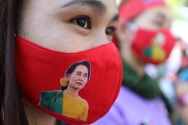 A close up of a Myanmar woman wearing a red face mask with a picture of Aung San Suu Kyi
