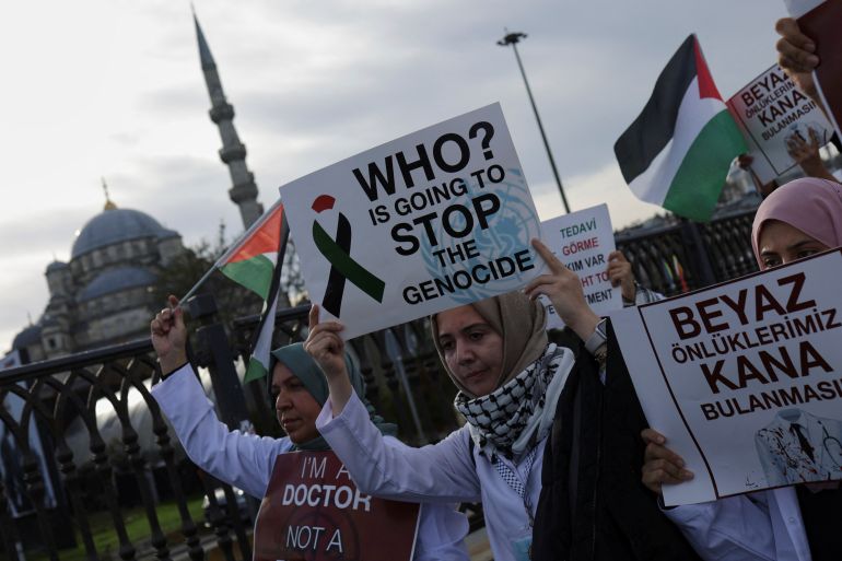 a woman in a white coat holds a sign saying who is going to stop the genocide