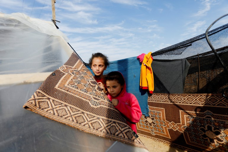 Displaced Palestinian girls, who fled their houses due to Israeli strikes, stand by a tent at a camp sheltering displaced people, in Rafah, in the southern Gaza Strip December 8