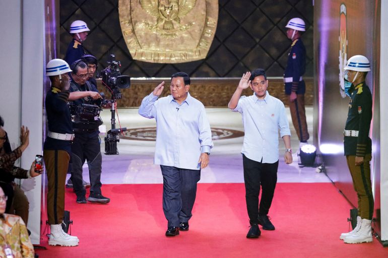 Indonesia's Defence Minister and presidential candidate, Prabowo Subianto, along with his running mate, Gibran Rakabuming Raka arrive for the debate. There are ceremonial guards on either side and a golden seal on the wall behind.