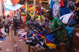 A woman selling second-hand clothes arranges several items at her stall while waiting for costumers in Owino, Kampala's largest second-hand clothes market.