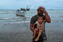 A newly-arrived Rohingya refugee holding a child gestures after arriving at Batee beach, Aceh province, Indonesia, on November 15, 2023. At least 147 Rohingya refugees, mostly women and children, landed in Indonesia's westernmost province on November 15, a local official said, a day after nearly 200 others came ashore in the same area. (Photo by CHAIDEER MAHYUDDIN / AFP)