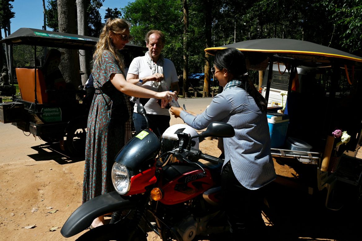 This photo taken on November 17, 2023 shows female Tuk Tuk driver Roeung Sorphy, aka Sopy, offering bottles of water to her passengers near the Bayon temple at the Angkor complex in Siem Reap province.