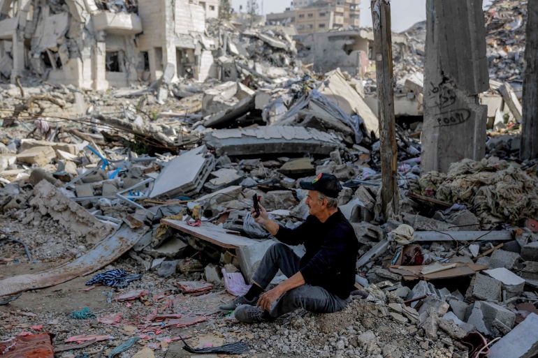 A Palestinian man uses his phone as he sits amid the rubble of destroyed buildings in Gaza City on the northern Gaza strip following weeks of Israeli bombardment, as a four-day ceasefire took effect on November 24, 2023. - The truce in the Israel-Hamas war began on November 24 and appeared to be holding, under a deal that will see hostages released in exchange for Palestinian prisoners. (Photo by Omar El-Qattaa / AFP)