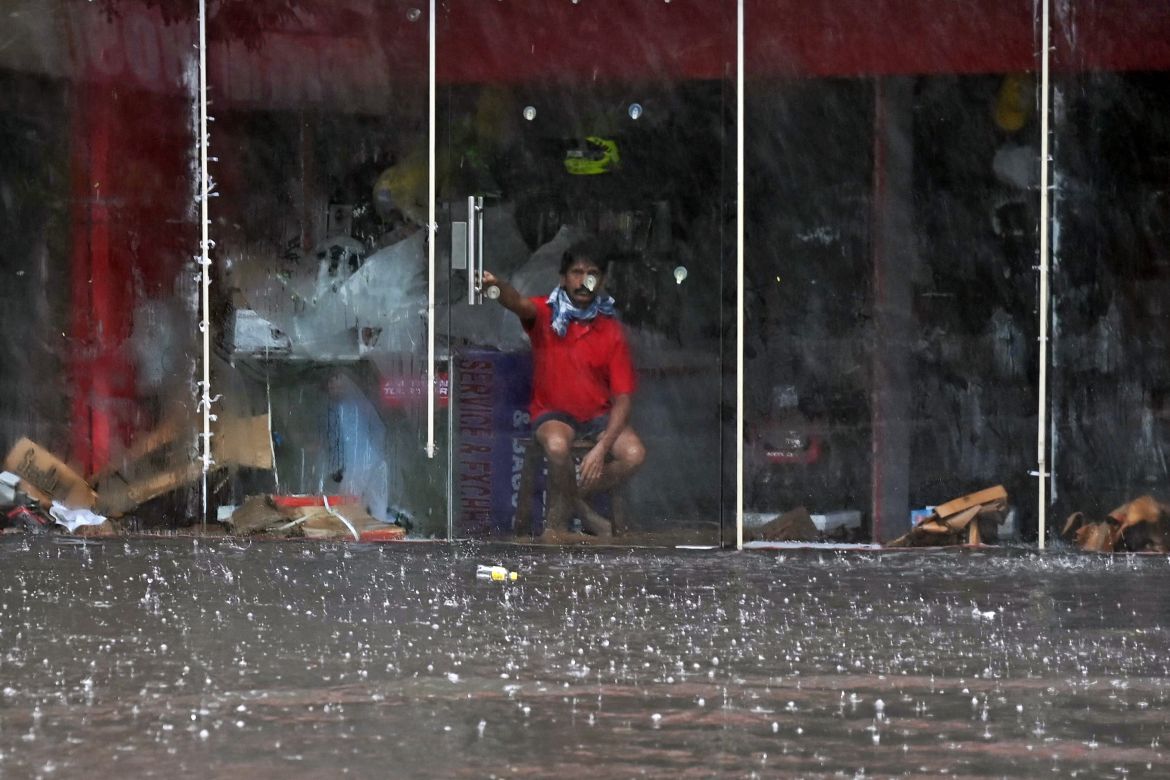 A worker sits inside a shop along a flooded street after heavy rains in Chennai on December 4