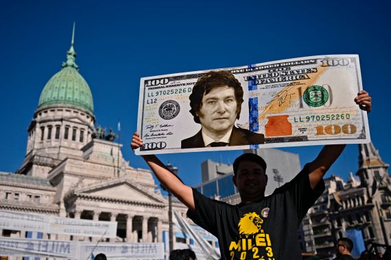 A supporter of Argentina's President-elect Javier Milei displays a one hundred dollar bill placard with an image of the future president as he waits outside the Congress before his inauguration ceremony, in Buenos Aires on December 10, 2023. - Javier Milei will on Sunday be sworn in as Argentina's president, as the country steels itself for harsh spending cuts and economic reforms aimed at curbing rampant inflation. (Photo by Luis ROBAYO / AFP)