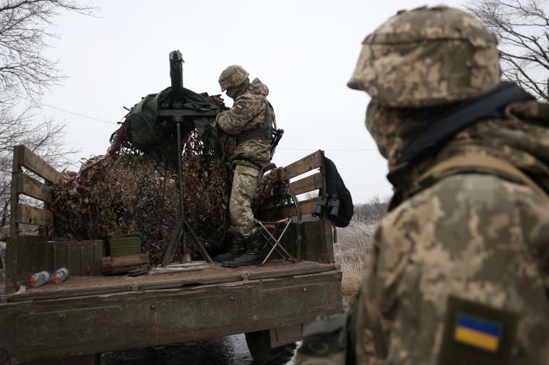 Two Ukrainian soldiers on the front line in Donetsk. One is on the back of a truck that is carrying a weapon