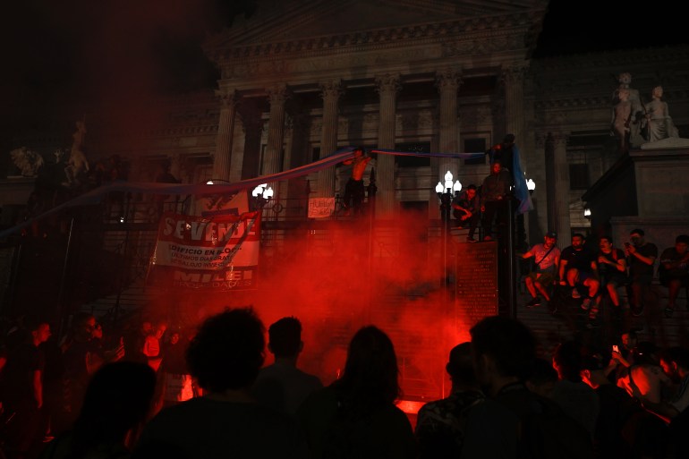 Protestors light a flare during a demonstration against the new government of Argentine President Javier Milei in front of the National Congress, in Buenos Aires on December 21, 2023. - Argentina's new leader Javier Milei on December 20, 2023 unveiled a series of measures to deregulate the country's struggling economy, eliminating or changing more than 300 rules via presidential decree, including on rent and labor practices. (Photo by Luis ROBAYO / AFP)