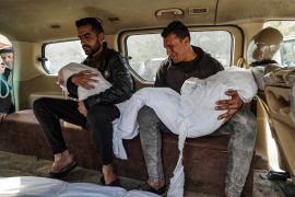 Two Palestinian men carry the shrouded bodies of their children, killed in Israeli bombardment, at Nasser hospital in Khan Younis on December 28, 2023 [AFP]