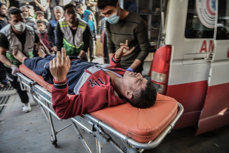 An injured Palestinian is brought into a hospital on a gurney following Israeli attacks in Khan Yunis, Gaza. Two men are wheeling the stretcher.