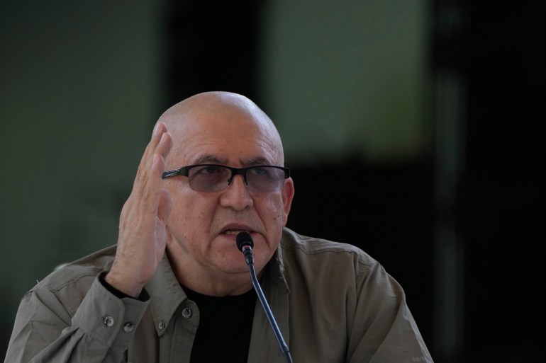 Antonio Garcia, a bald man with dark-rimmed glasses and an olive-colored shirt, gestures with his hands as he speaks into a microphone.
