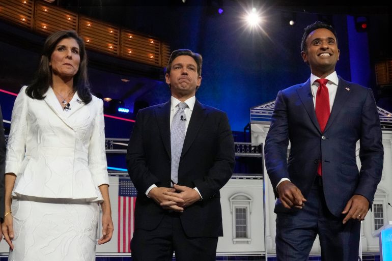 Nikki Haley, Ron DeSantis and Vivek Ramaswamy stand side by side on a debate stage in Miami Florida. The two men wear blue suits, while Haley wears a white suit.