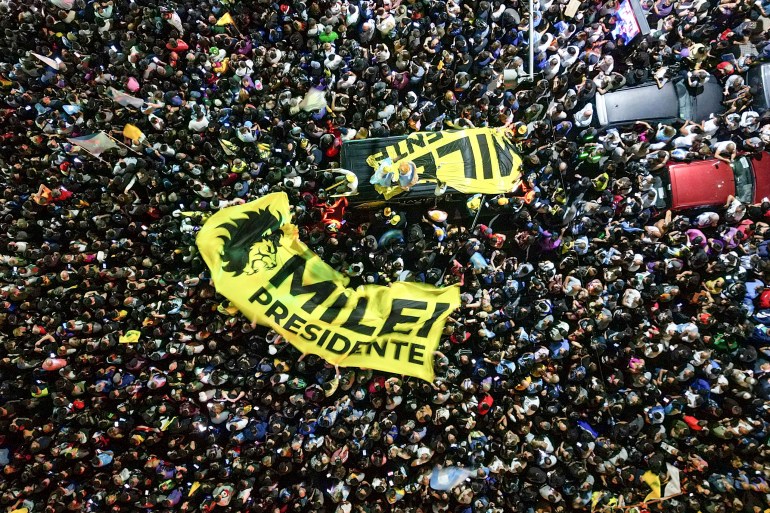 A crowd of Milei supporters, seen from above, hold up yellow banners that read, "Milei presidente".