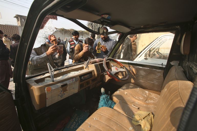 Members of media film and taking photo of a damaged van at the site of a bomb explosion, in Peshawar, Pakistan, Tuesday, Dec. 5, 2023. A roadside bomb went off near a school in northwestern Pakistan on Tuesday, wounding passersby and damaging windows of a nearby bank and several shops, authorities said. (AP Photo/Muhammad Sajjad)