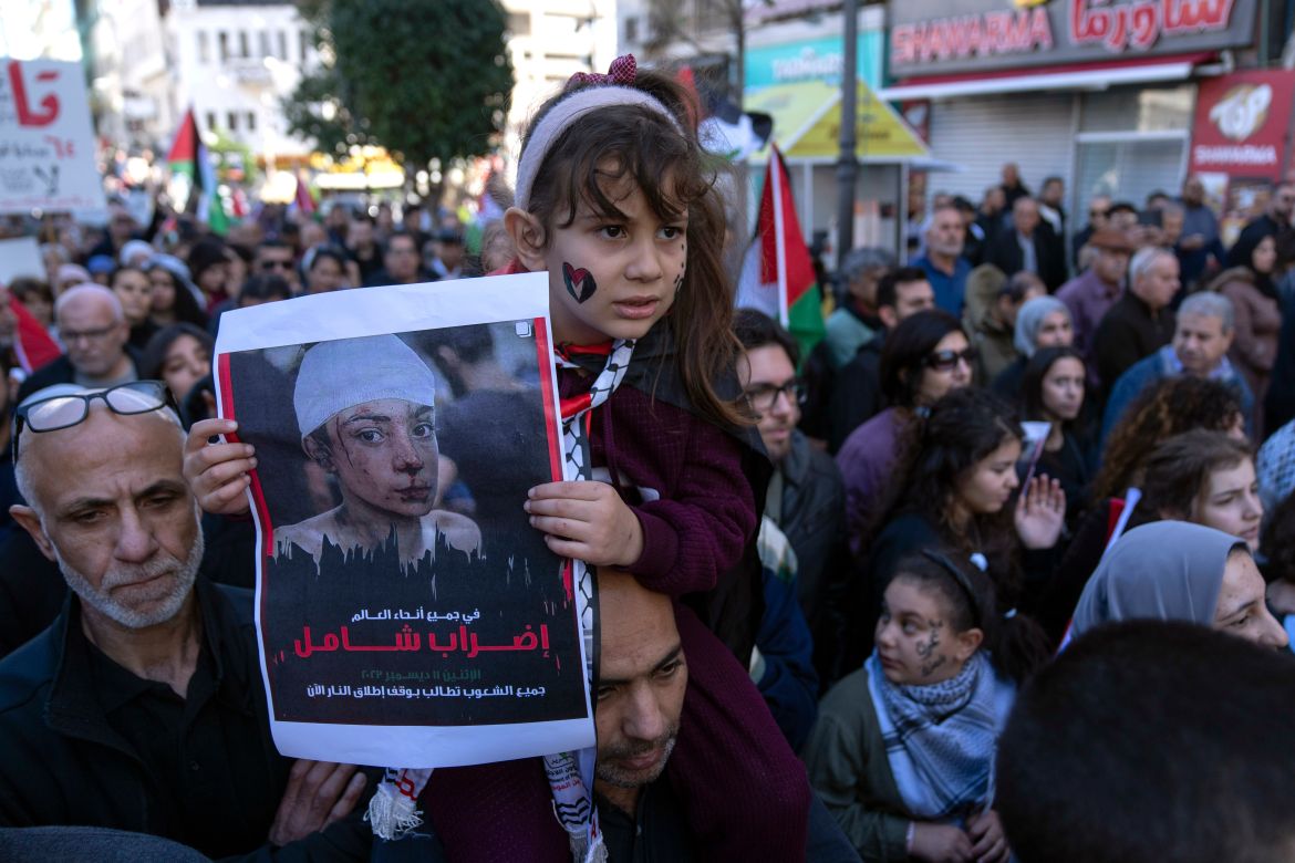 A girl carries a poster with Arabic writing that reads "a general strike in all over the world," during a rally in solidarity with Gaza, in the West Bank city of Ramallah, Monday, Dec. 11