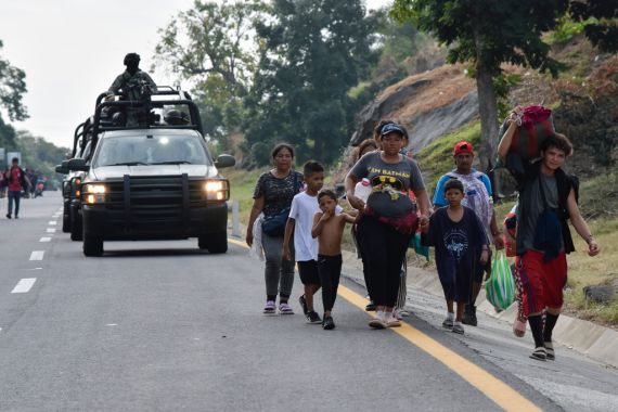 A family walks down the road with a convoy of soldiers behind them